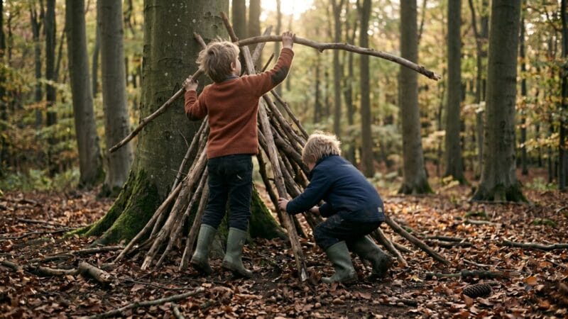 Naturaktiviteter for børn: sjove idéer til hele året To børn bygger en hule af grene i en dansk bøgeskov