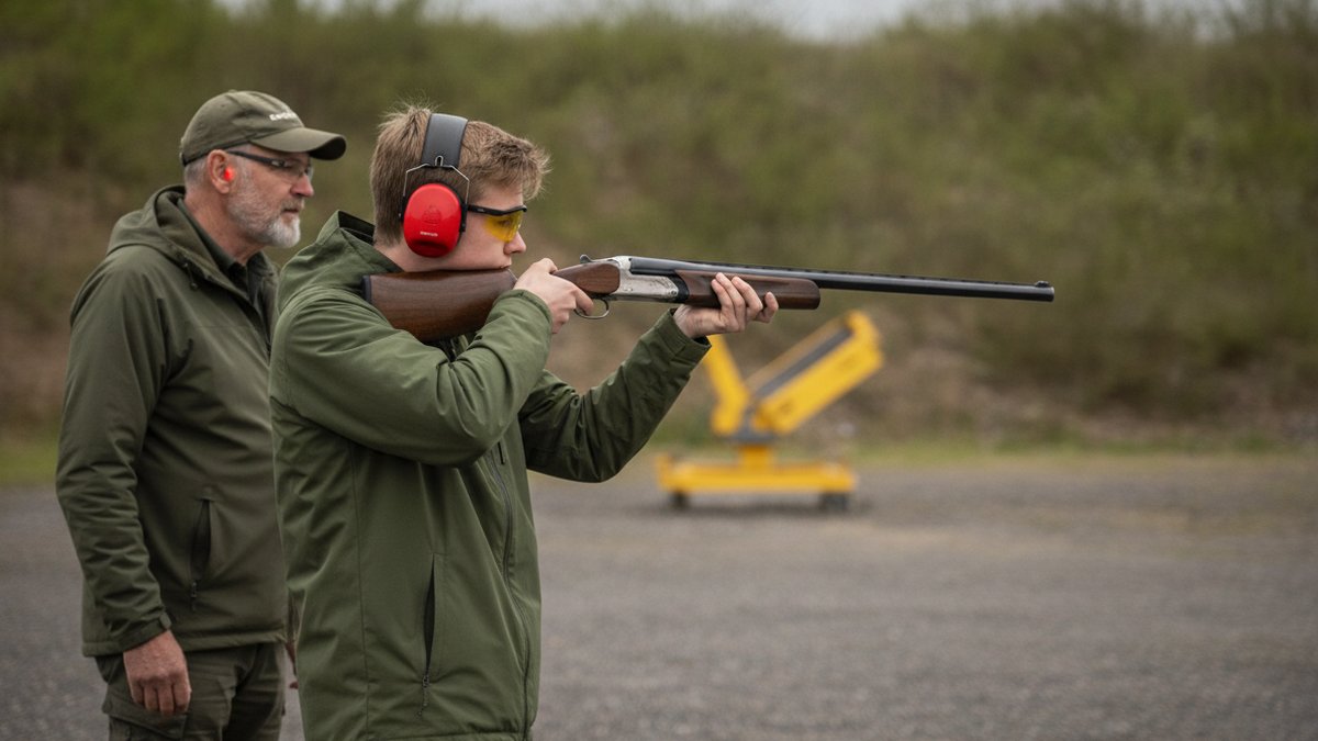 Jagt for begyndere: jagttegn, priser og dit første grej 1 Nyjæger med instruktør på skydebane med haglgevær, høreværn og skydebriller under jagttegnskursus
